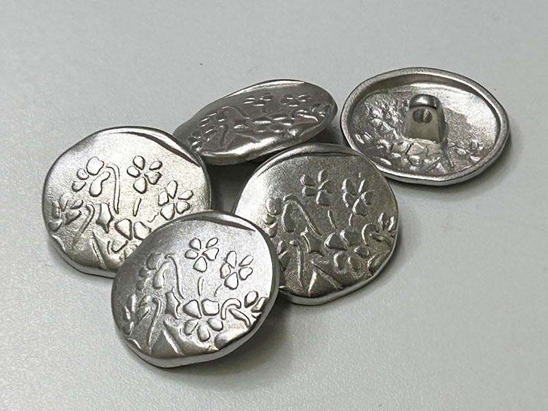 Verspielte, unrunde Metallknöpfe in Silber mit Blumenmotiv und Ösenbefestigung