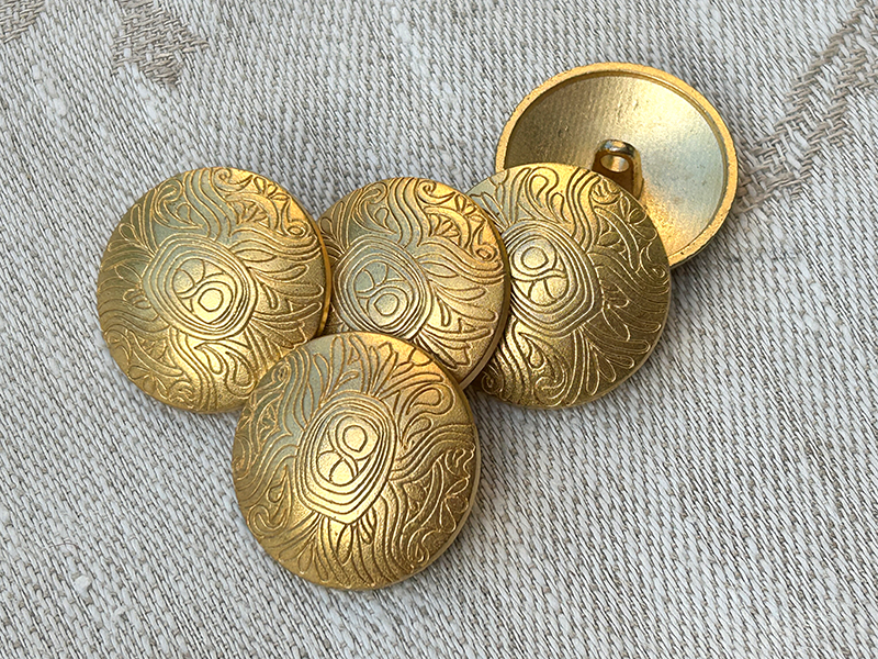 Goldfarbene Metallknöpfe mit ornamental vertieftem Linienmuster