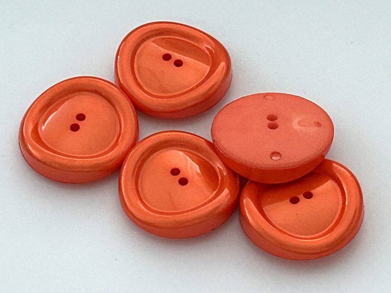 Schillernde orangefarbene Kunststoffknöpfe in besonderer Form
