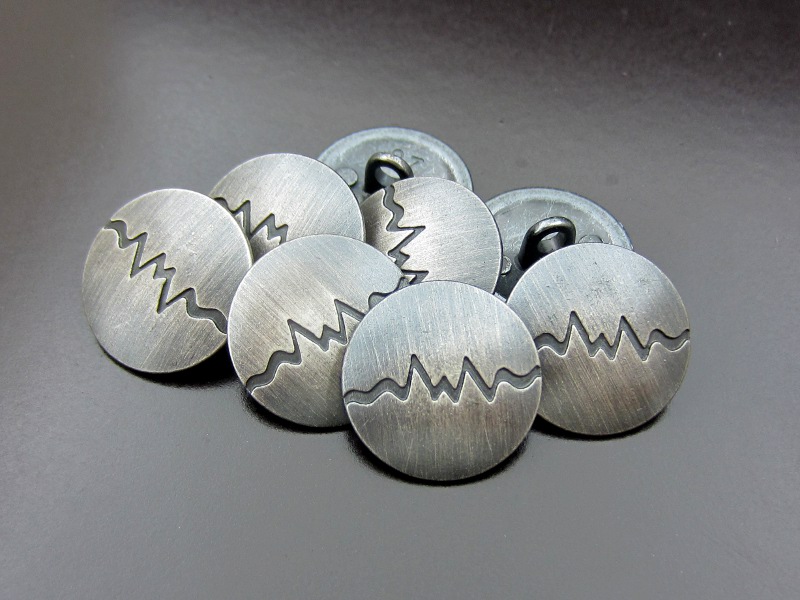 Stahlfarbener Metallknopf mit Kurve
