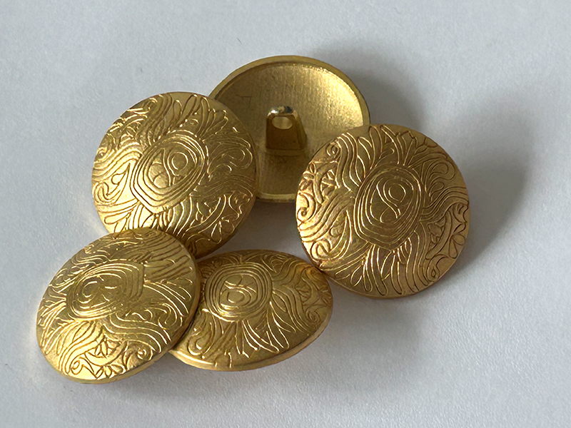 Goldfarbene Metallknöpfe mit ornamental vertieftem Linienmuster