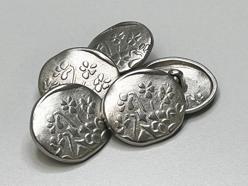 Verspielte, unrunde Metallknöpfe in Silber mit Blumenmotiv und Ösenbefestigung